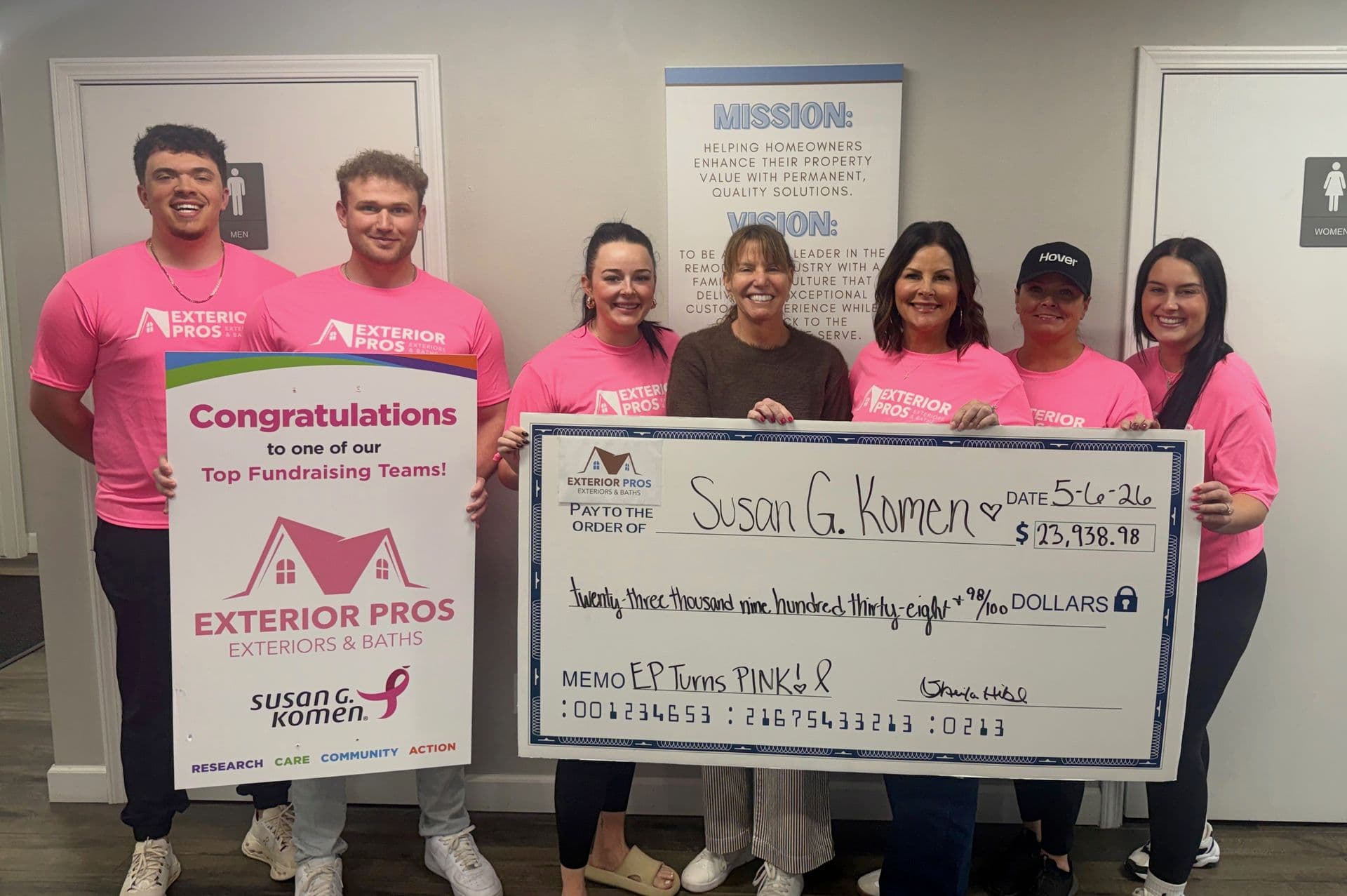 Exterior Pros team in pink shirts holding oversized check for $123,138.18 donated to Susan G. Komen, congratulated as top fundraising team