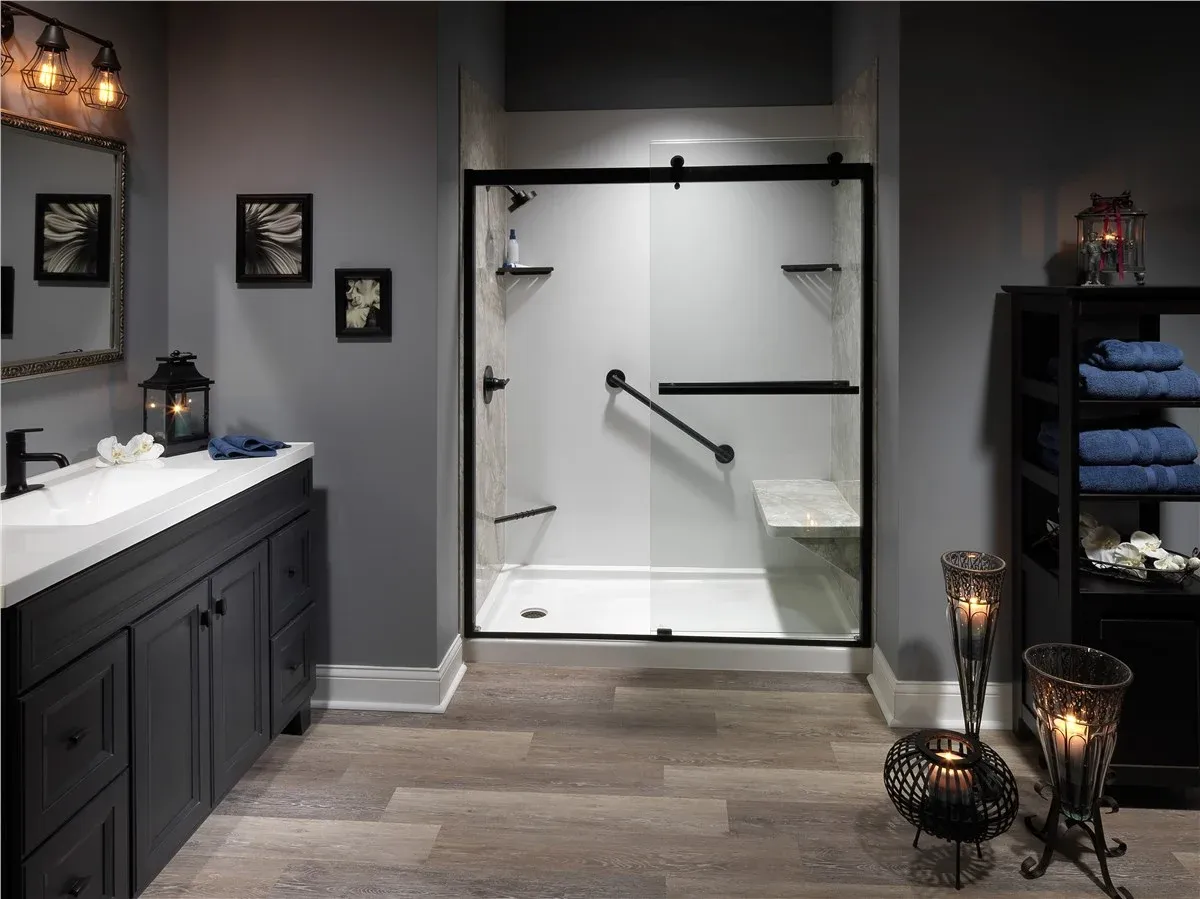 Modern bathroom with black-framed sliding glass shower door, white vanity with blue towels, wall art, decorative lighting, and shelving with blue towels and candles