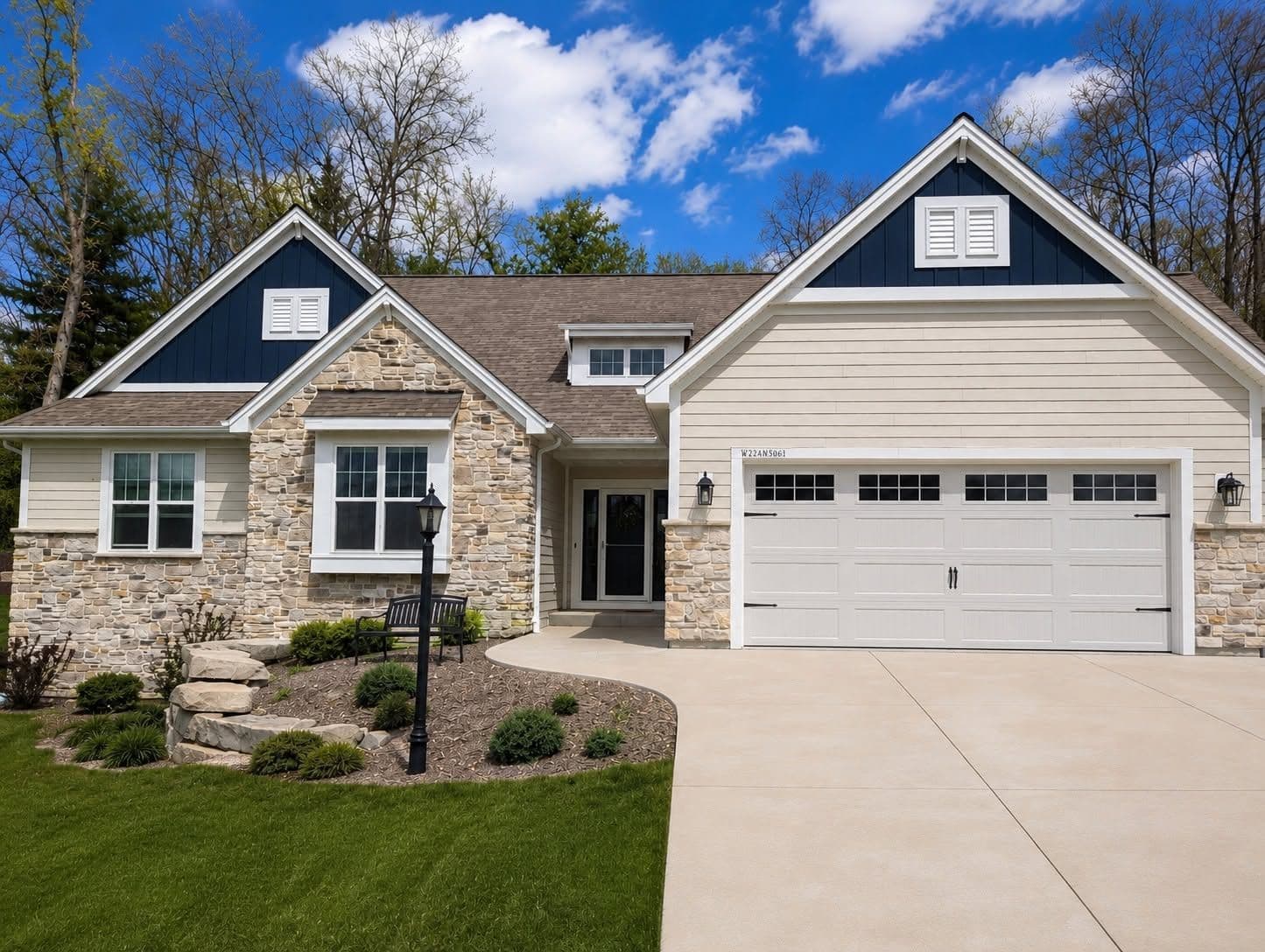 Modern two-story home with stone and siding exterior, two-car garage, front porch with black lamp post, manicured landscaping, and driveway