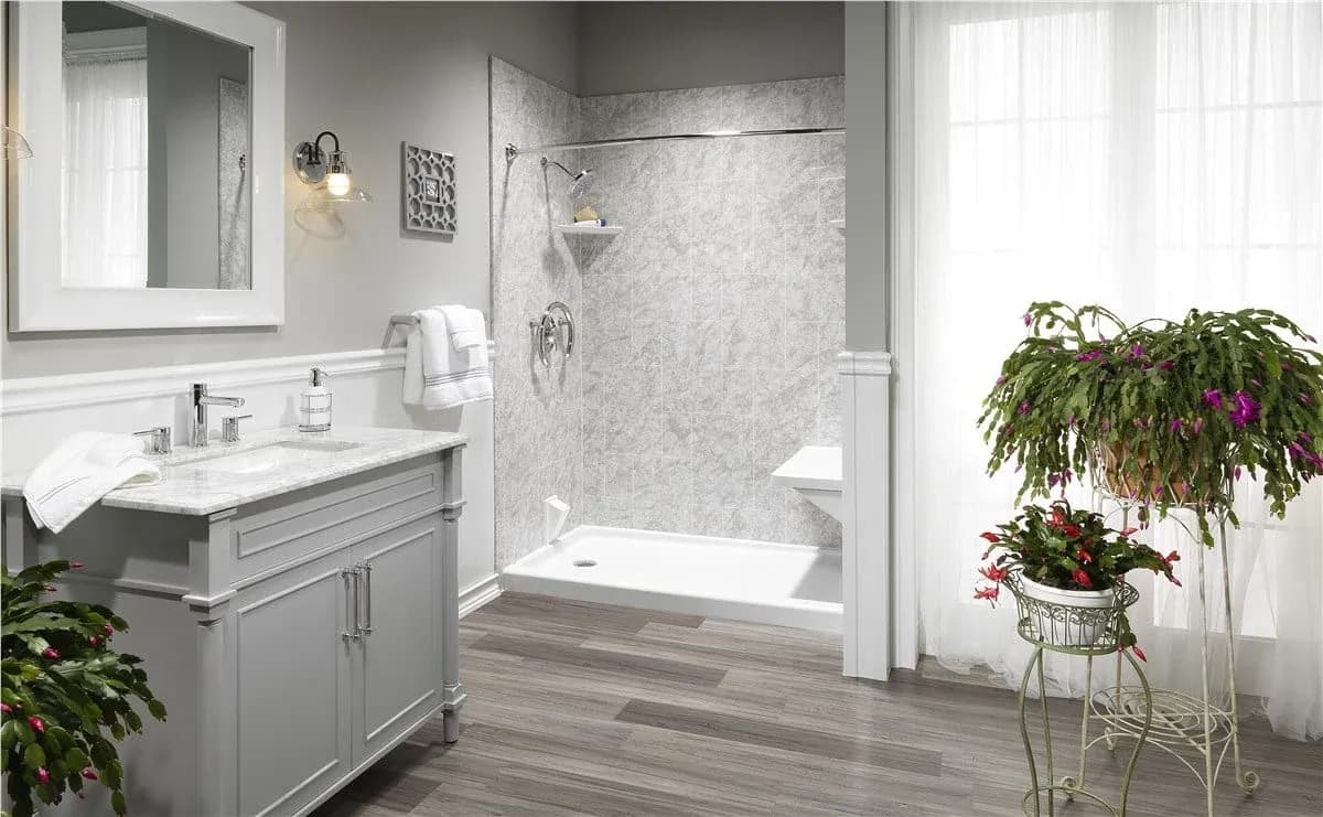 Modern bathroom with gray vanity, marble shower enclosure, wood-look flooring, and potted flowering plants near the window