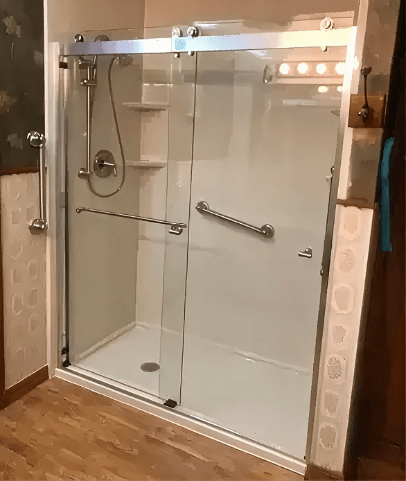 Frameless glass sliding shower enclosure with chrome fixtures and grab bars installed in a bathroom