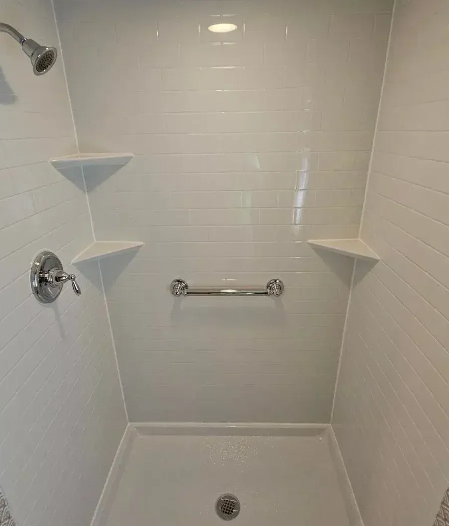 Newly renovated white tile shower enclosure with rainfall showerhead, corner shelves, grab bar, and recessed lighting