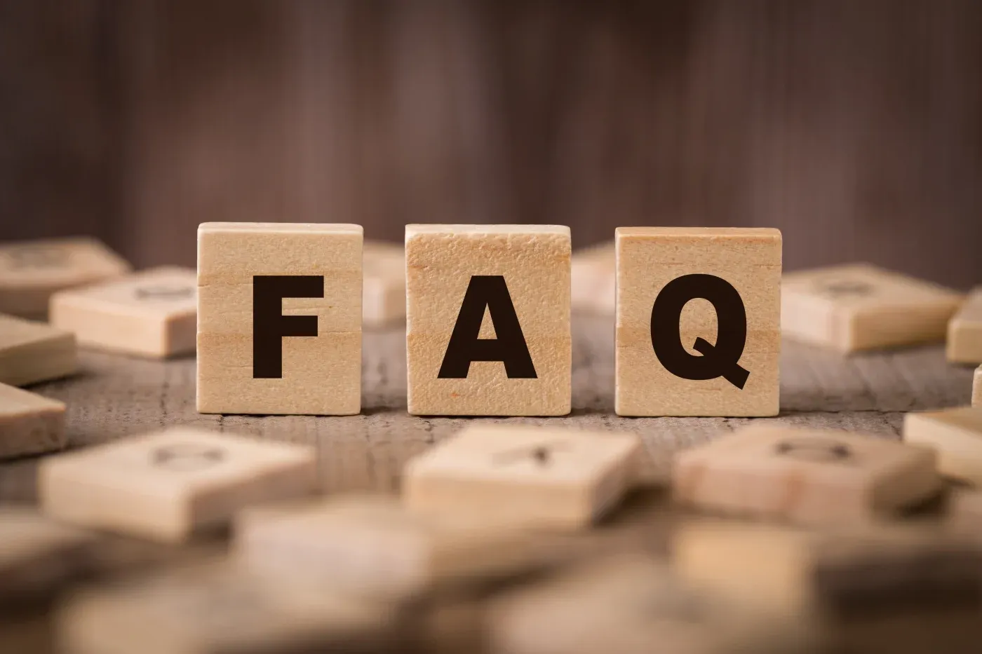 Three wooden blocks spelling FAQ surrounded by scattered letter tiles
