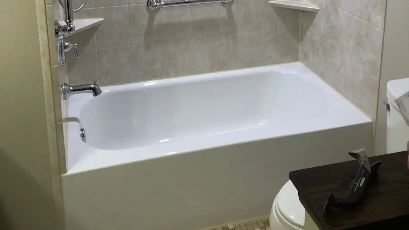 White rectangular bathtub with chrome fixtures and glass shower enclosure in a tiled bathroom