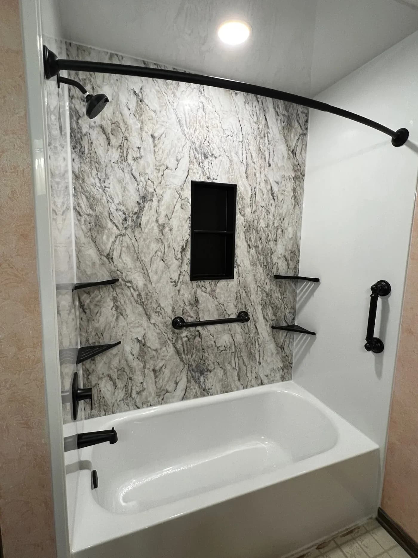 Modern bathroom shower with white soaker tub, marble tile walls, black fixtures and curved glass door enclosure
