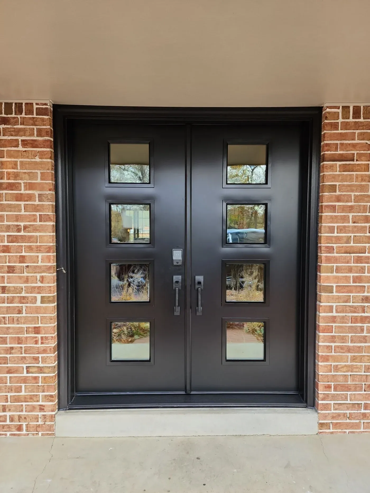 Modern black double entry doors with eight small windows set in red brick facade with concrete entrance