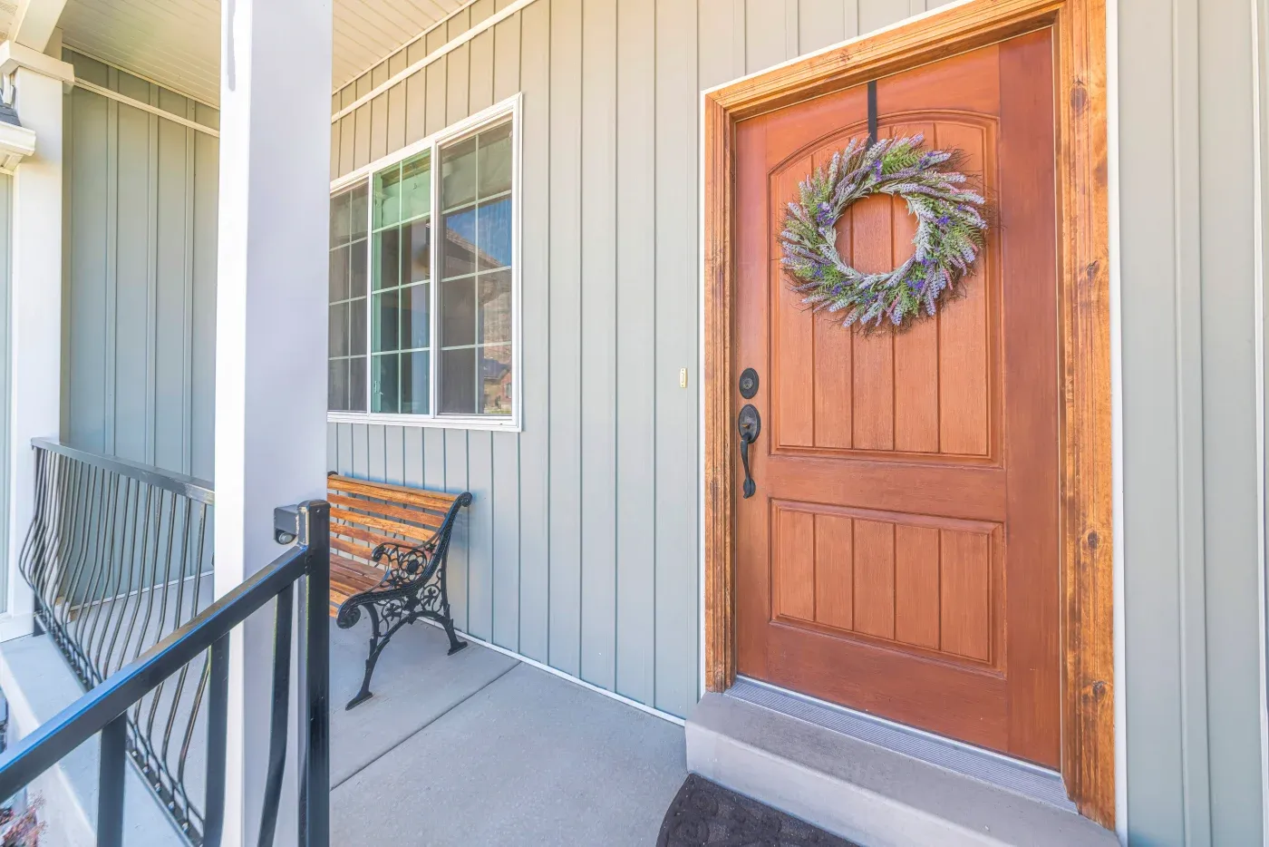 Front porch with red wooden door decorated with purple and green wreath, wooden bench, and metal railing