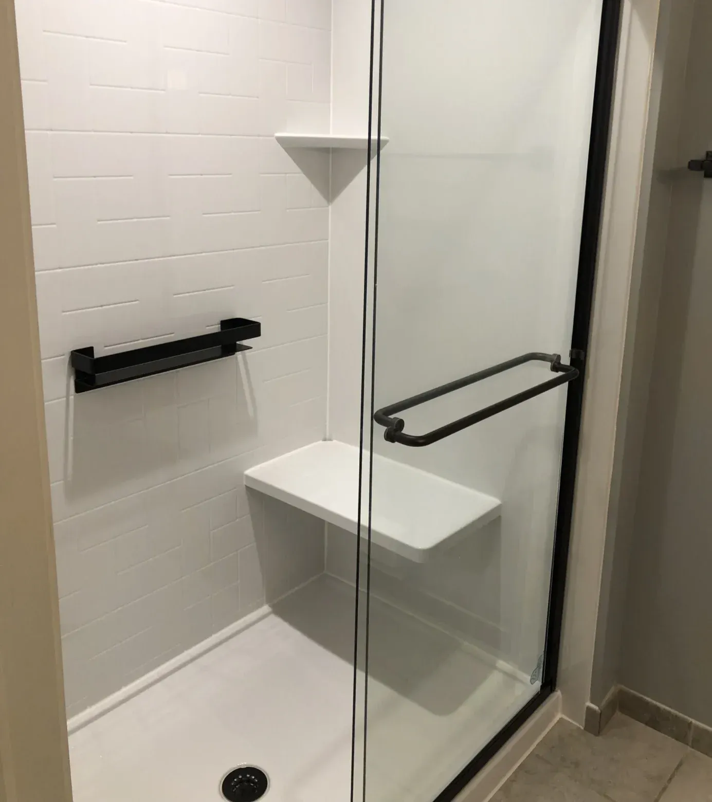 Modern shower enclosure with white subway tile walls, glass door with black frame, built-in white shelf, black towel bar, and corner soap dish