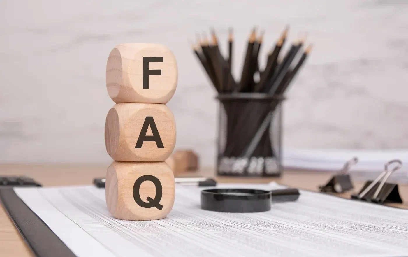 Wooden blocks stacked vertically spelling FAQ on a desk with office supplies in the background