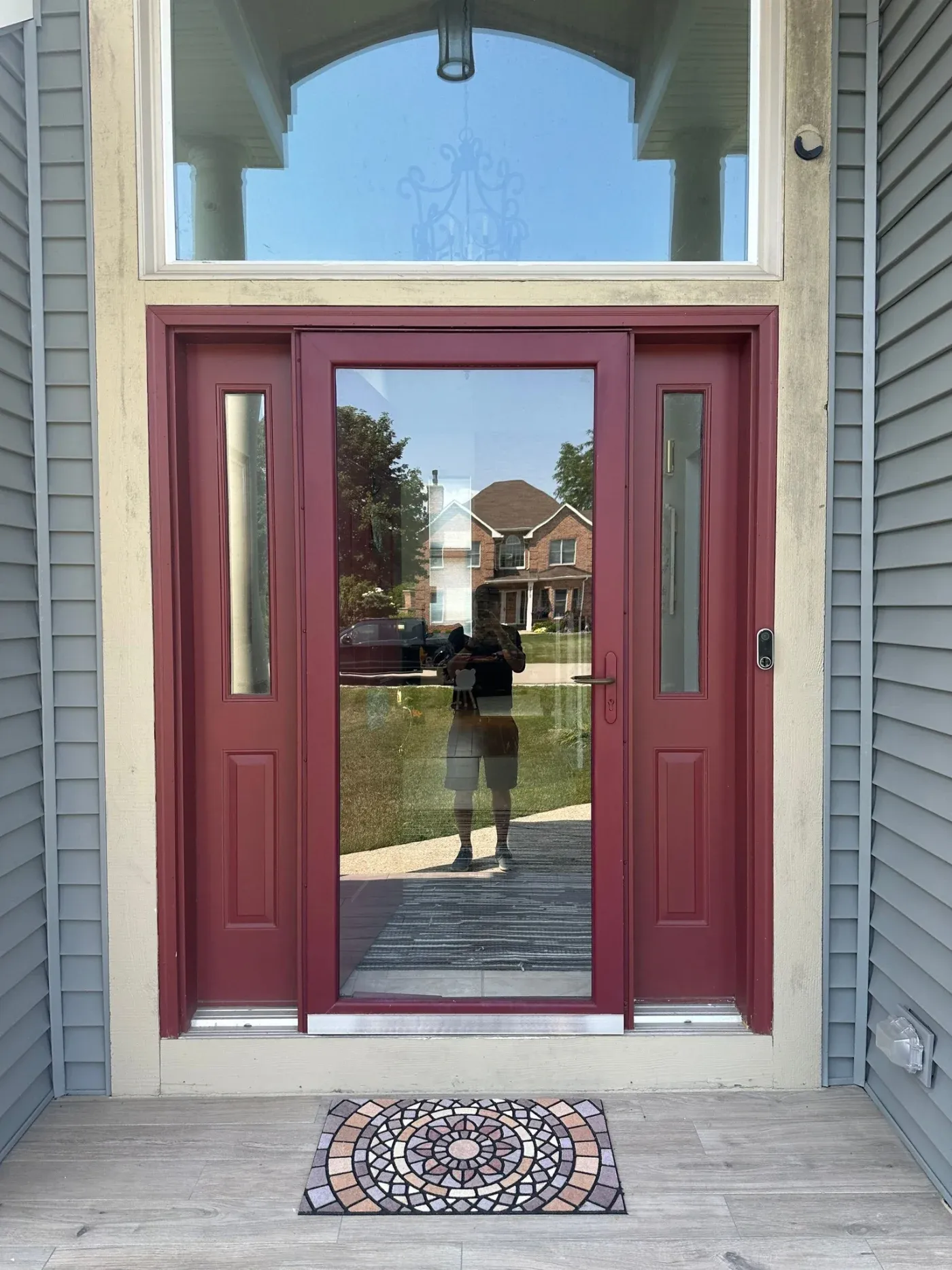 Burgundy double entry doors with sidelights and transom window, view through to residential street and brick house beyond