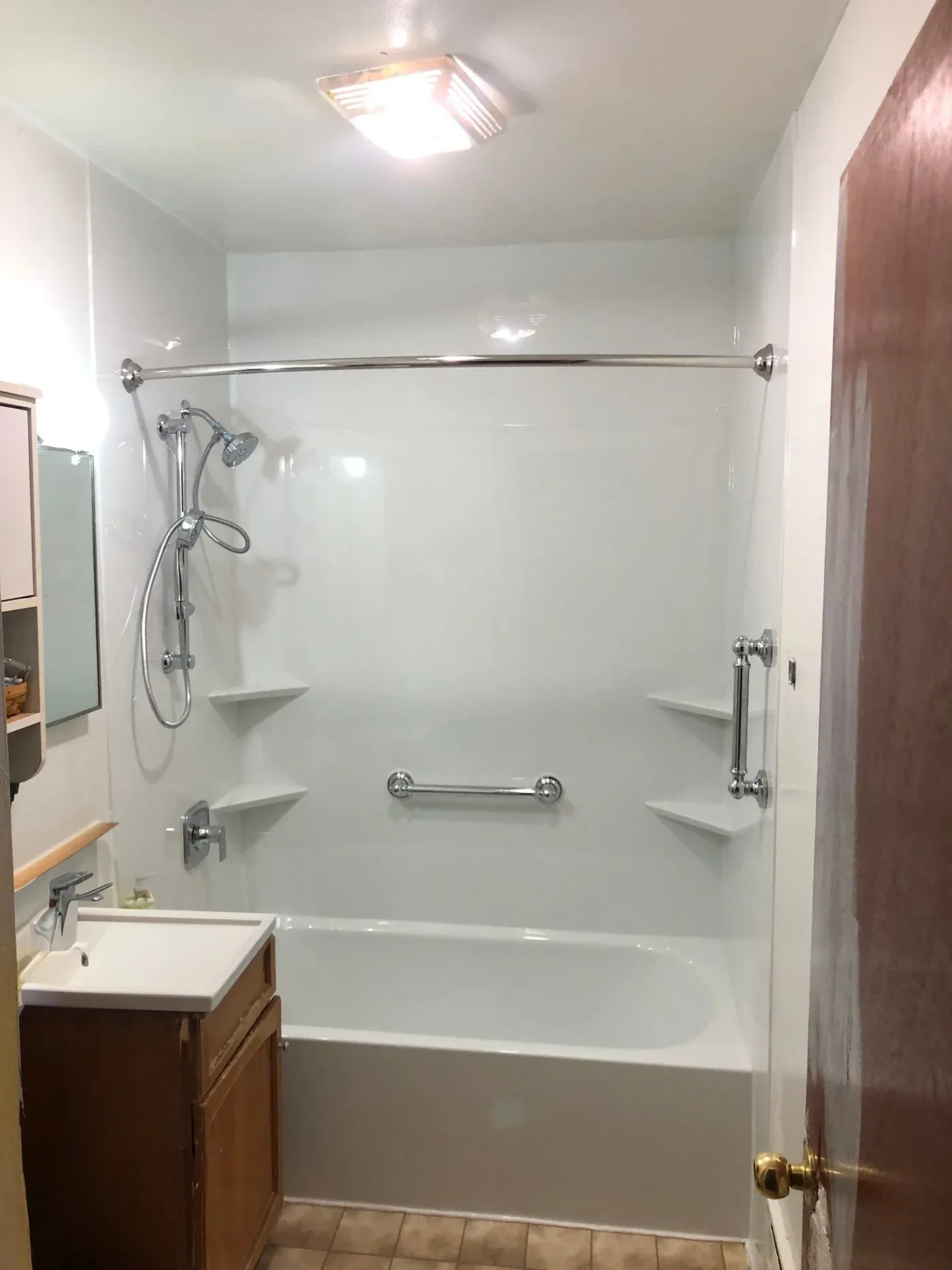 Bathroom with white tile shower enclosure featuring showerhead, handrails, and built-in shelves, wooden vanity sink on left, and large mirror