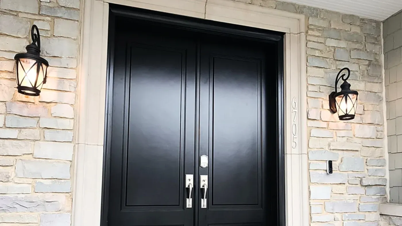 Black double entry doors with chrome handles flanked by tan brick walls and symmetrical black lantern sconces