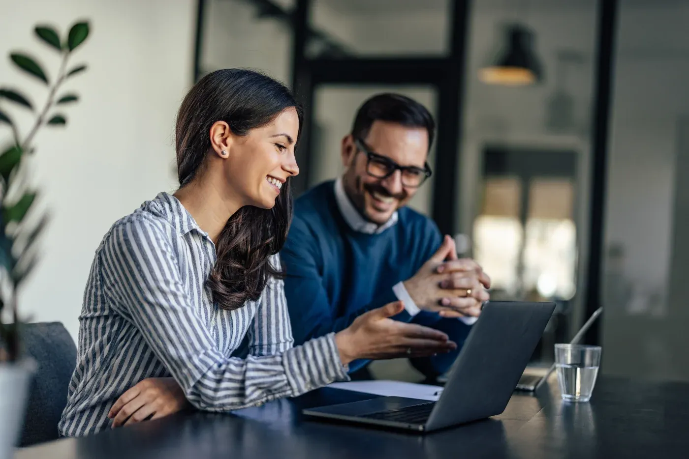 Two colleagues collaborating at a laptop in a modern office, smiling while reviewing content together