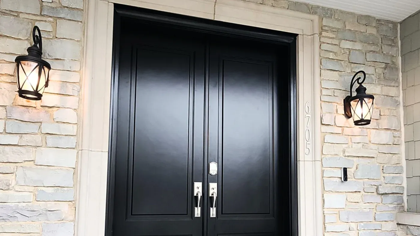 Double black front doors with silver handles flanked by tan brick walls, black lantern lights, and house number 670