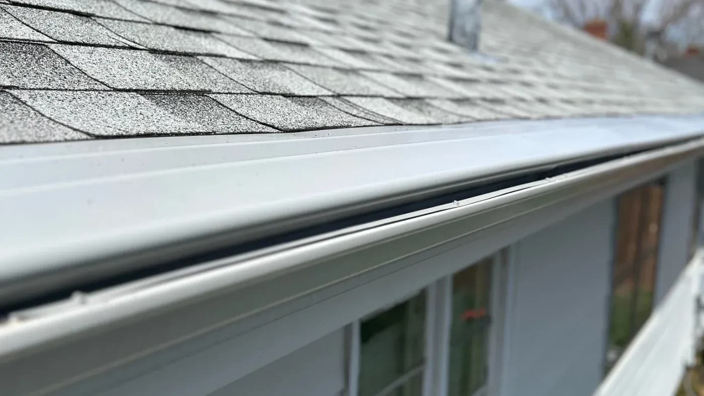 Close-up of gutter system where white aluminum gutter meets asphalt shingle roof edge