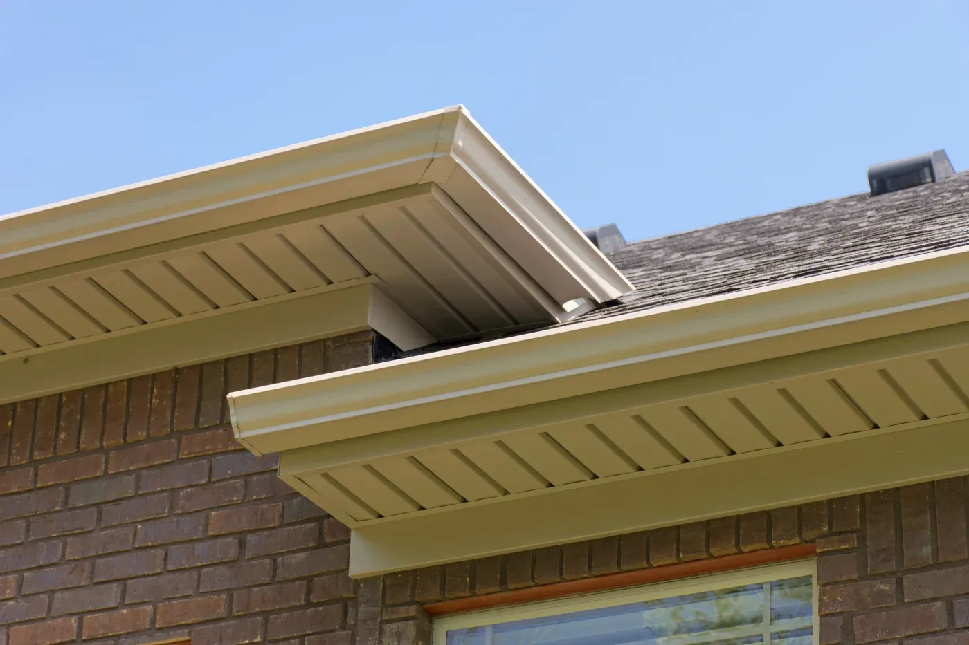 Cream-colored soffit and fascia with vented panels on brick residential home exterior against blue sky
