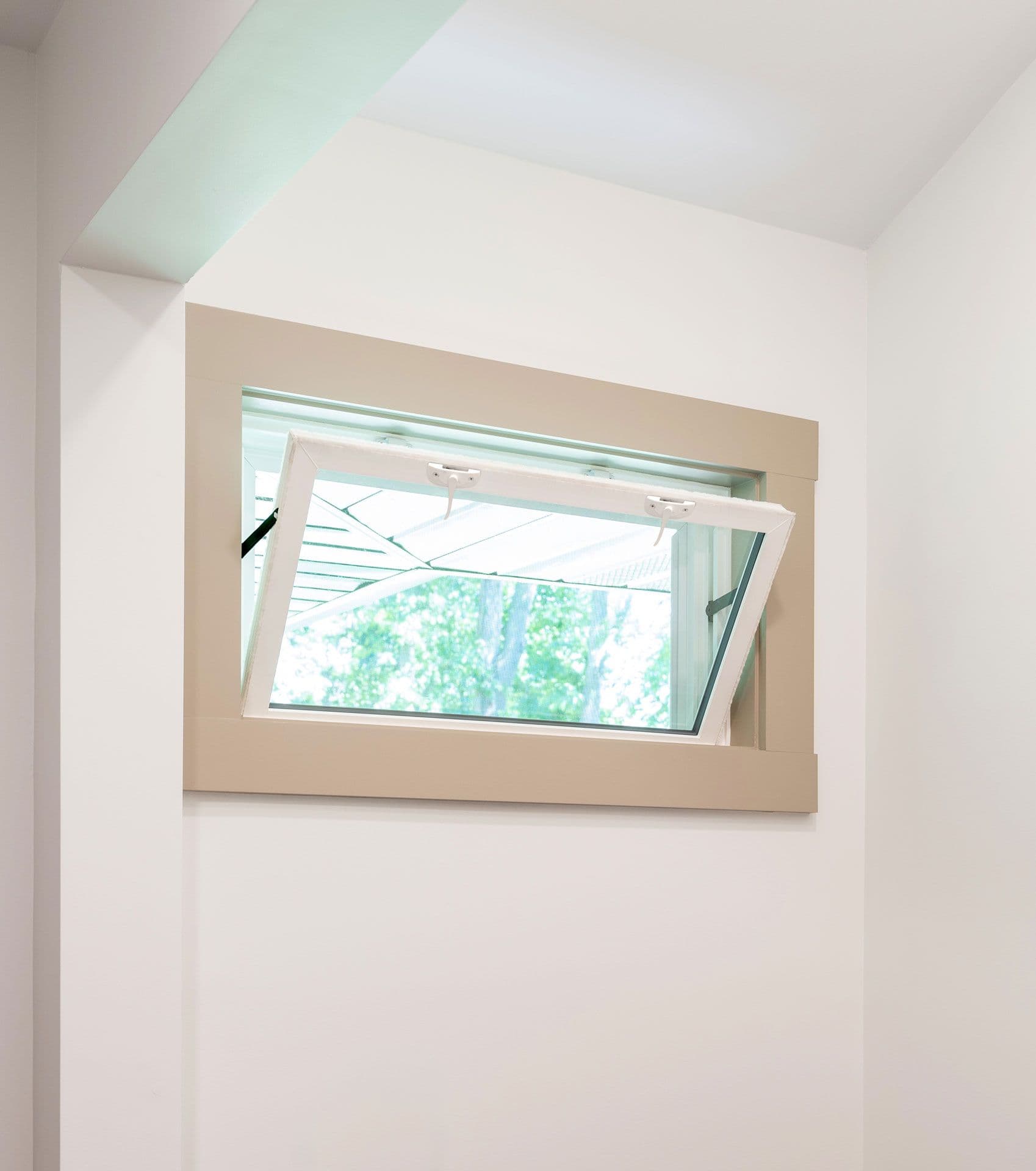 Open hopper window with white frame showing green trees outside