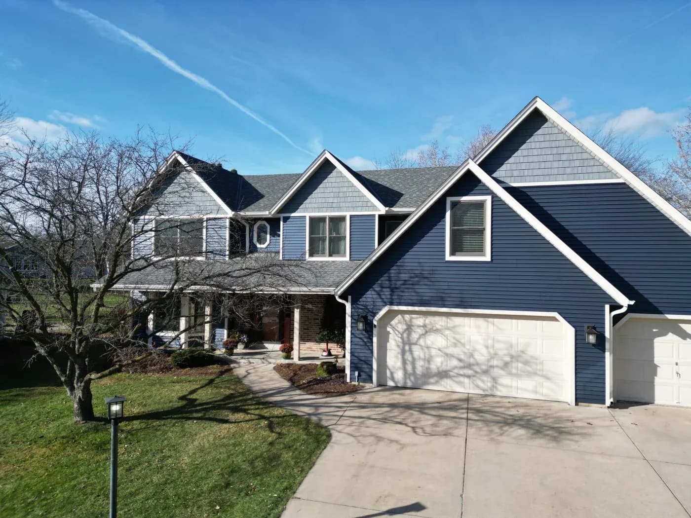 Two-story blue and white residential home with attached white garage, front porch, multiple gabled rooflines, and landscaped lawn under clear blue sky