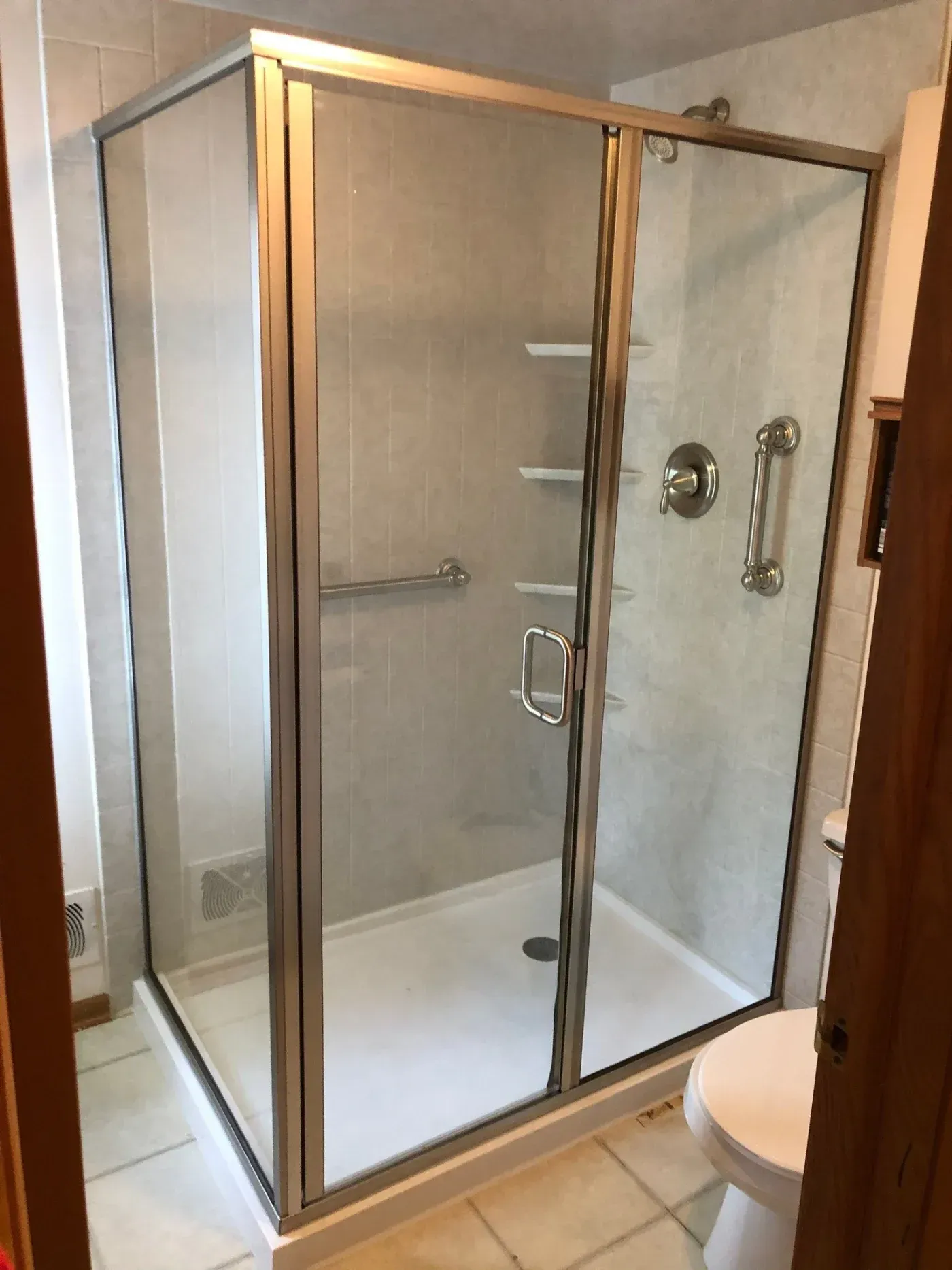 Frameless glass shower enclosure with brushed nickel fixtures, white subway tile surround, and built-in shelving inside a bathroom