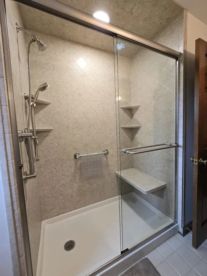Frameless glass shower enclosure with diagonal tile pattern, built-in shelving, handheld and overhead showerheads, and grab bar