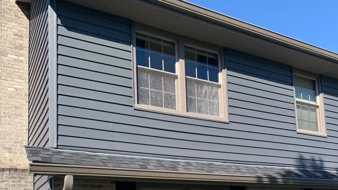 Building exterior with blue horizontal siding, cream-colored window frames, and brick chimney detail under clear sky