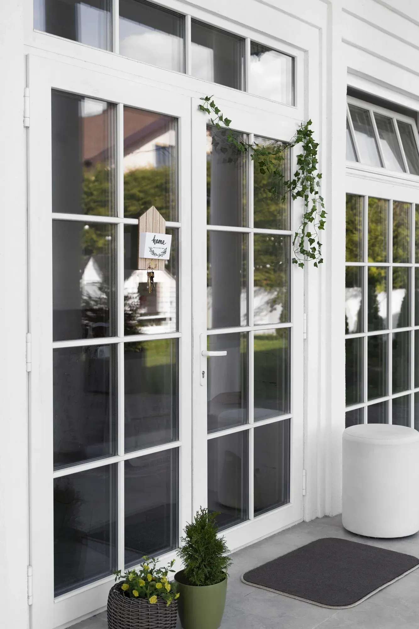 White French patio doors with glass panes, transom windows, climbing greenery, and potted plants.