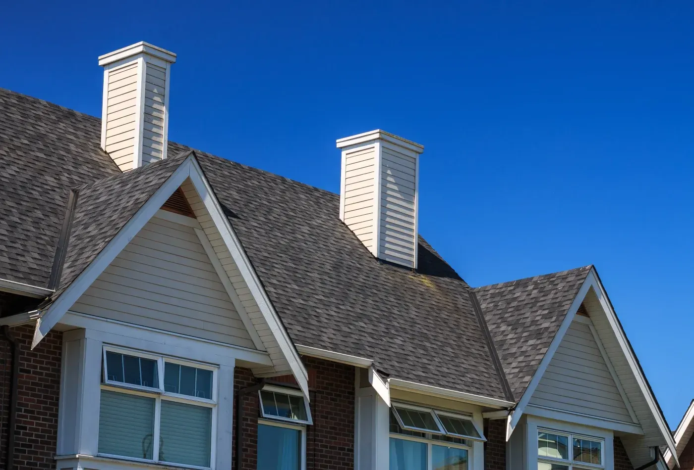 Close-up of a residential asphalt shingle roof with multiple gables and chimney structures in Ashippun, Wisconsin.