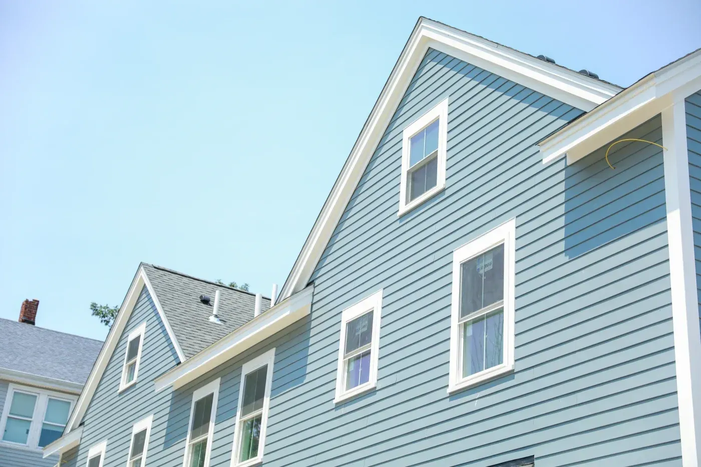 Blue-gray house exterior with horizontal vinyl siding, white trim, and several windows.