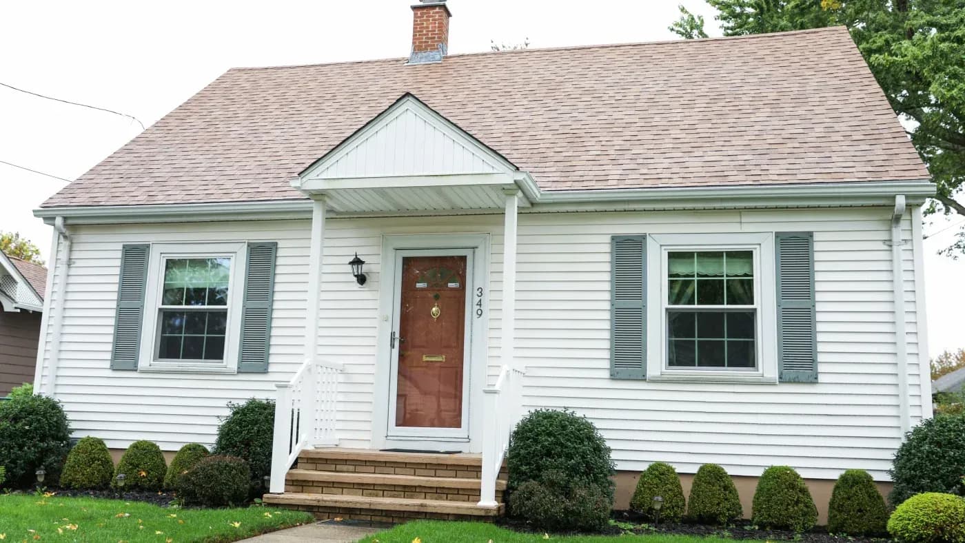 White home with tan asphalt shingle roofing, front porch, and landscaped yard in Ashippun, Wisconsin.