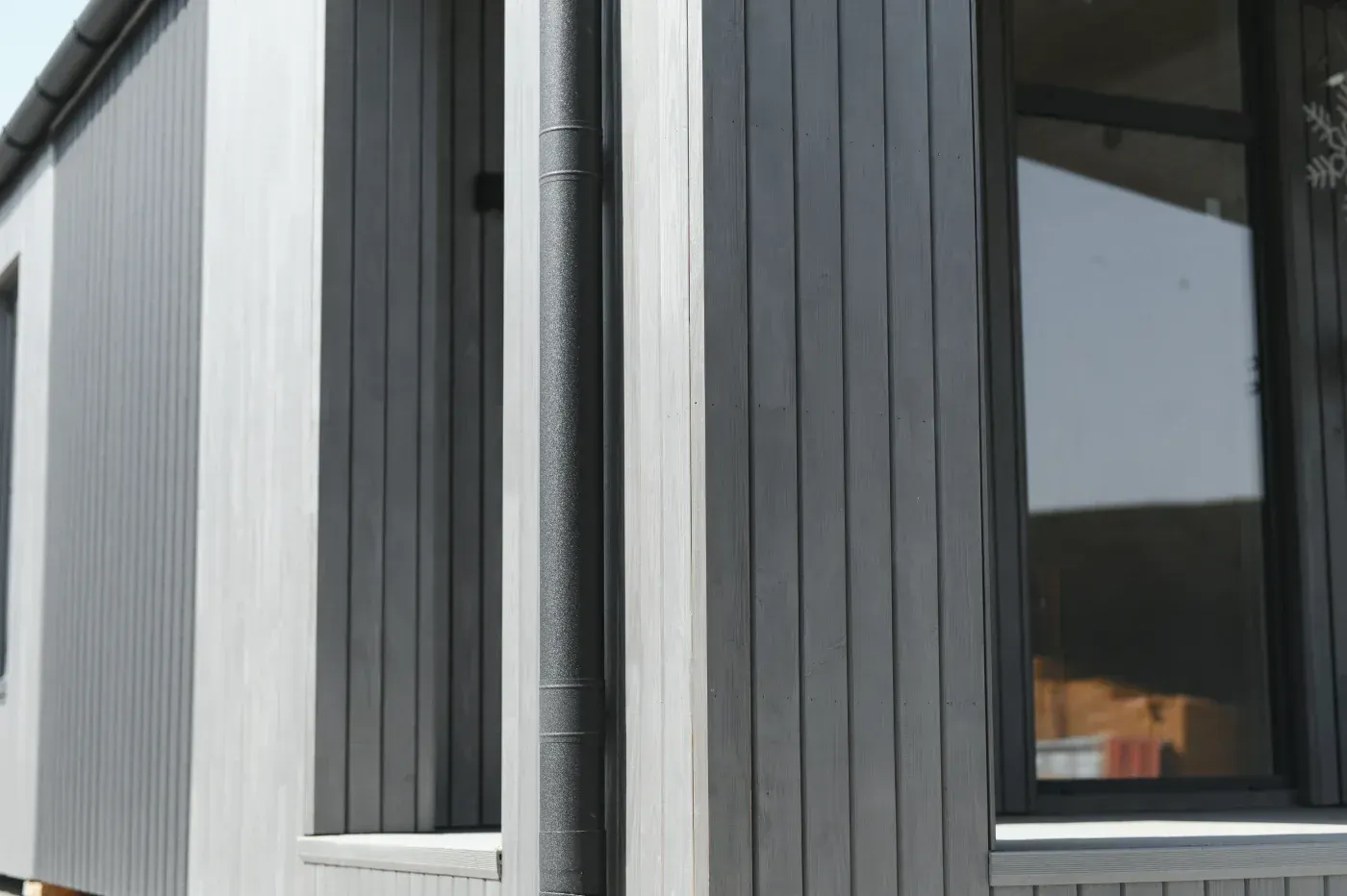 Modern home exterior with black vertical board-and-batten siding, white trim, and black gutters.
