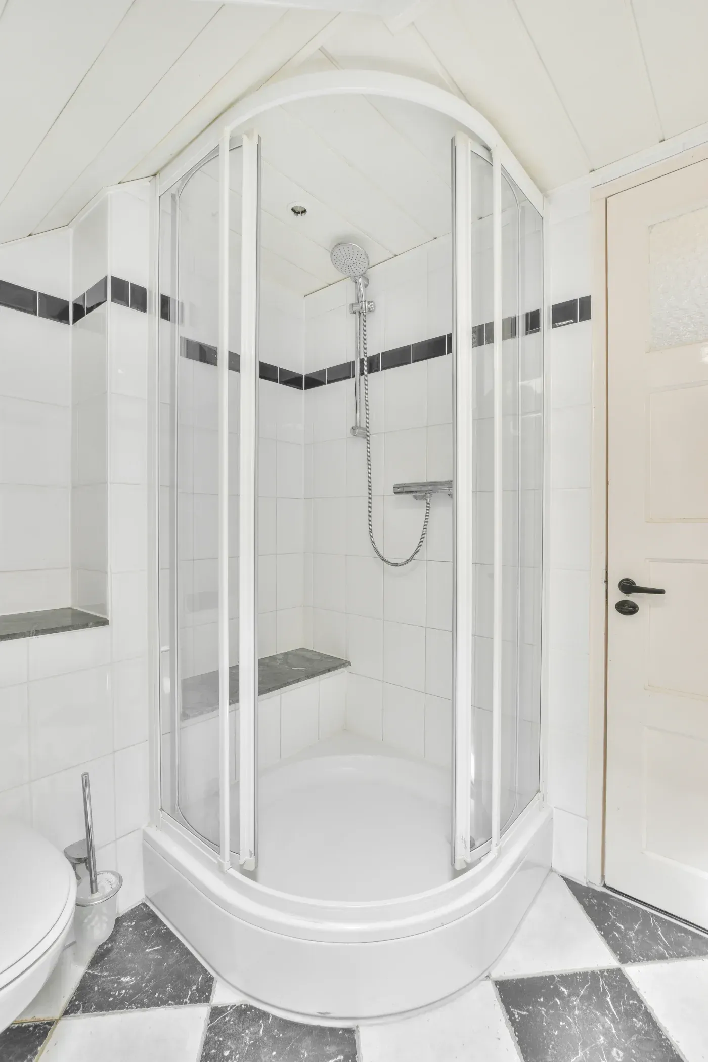 Curved corner shower with clear glass doors, white tile, handheld showerhead, and built-in seating.