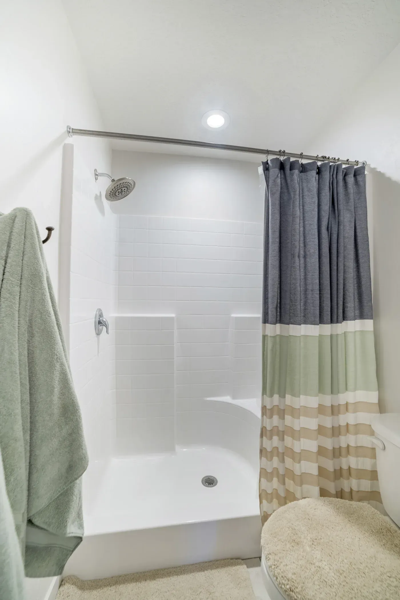 Modern bathroom shower enclosure with white subway tile walls, rainfall showerhead, and gray striped shower curtain with green and tan color-block pattern on metal rod