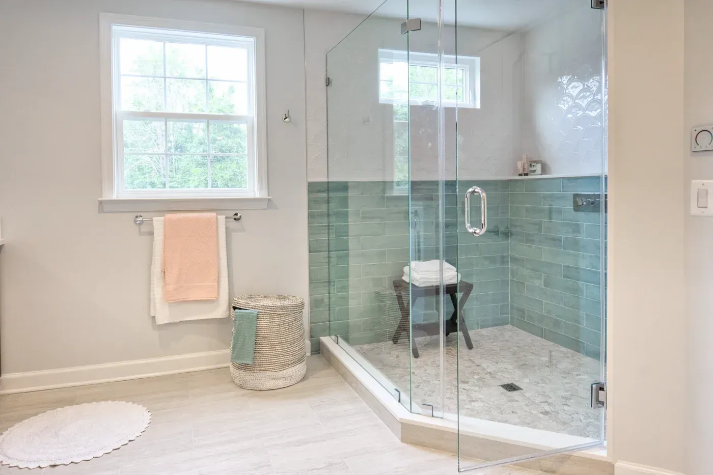 Spacious glass-enclosed walk-in shower with aqua tile walls, mosaic flooring, and a shower bench.