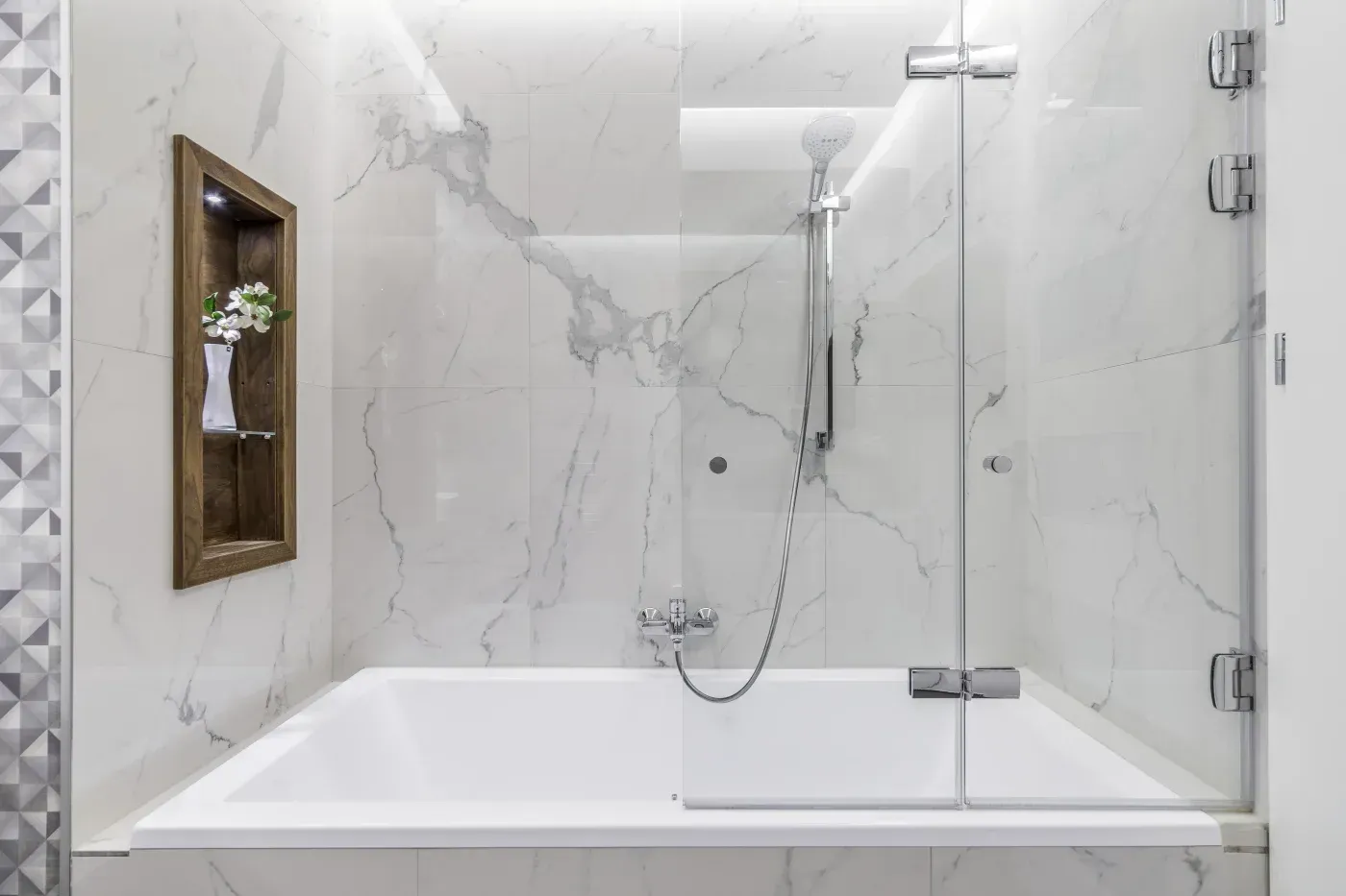 Modern bathtub and shower combination with marble-look walls, glass enclosure, and handheld showerhead.