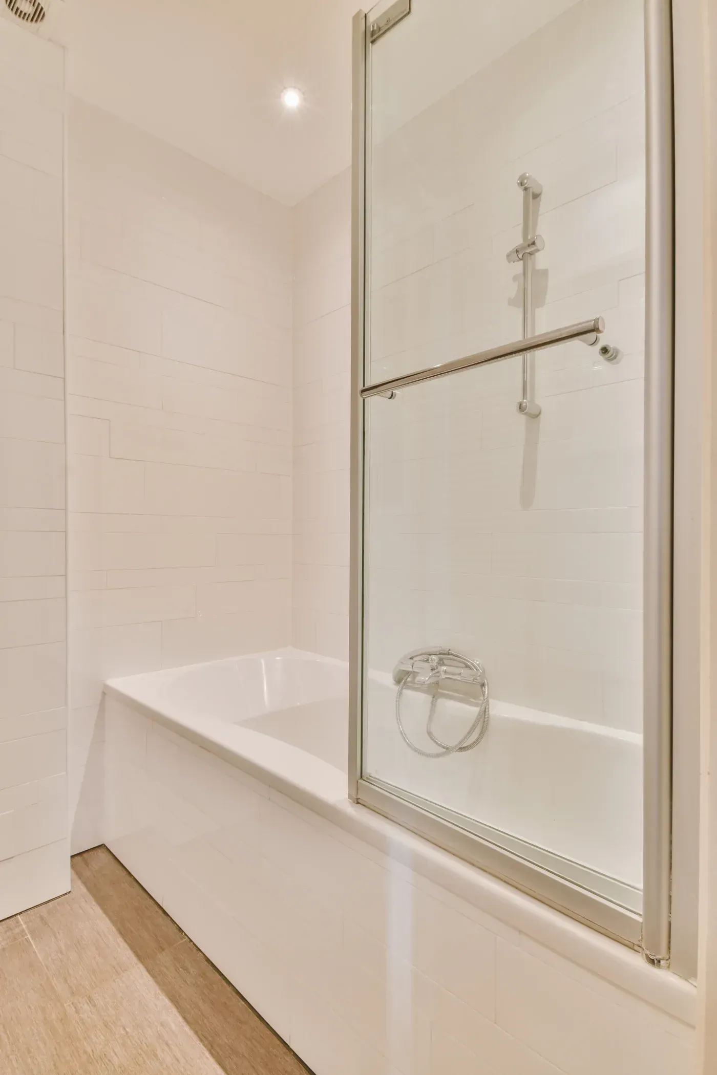 Bathroom with white subway tile walls, built-in bathtub on left, and glass shower door with silver hardware and handhold on right