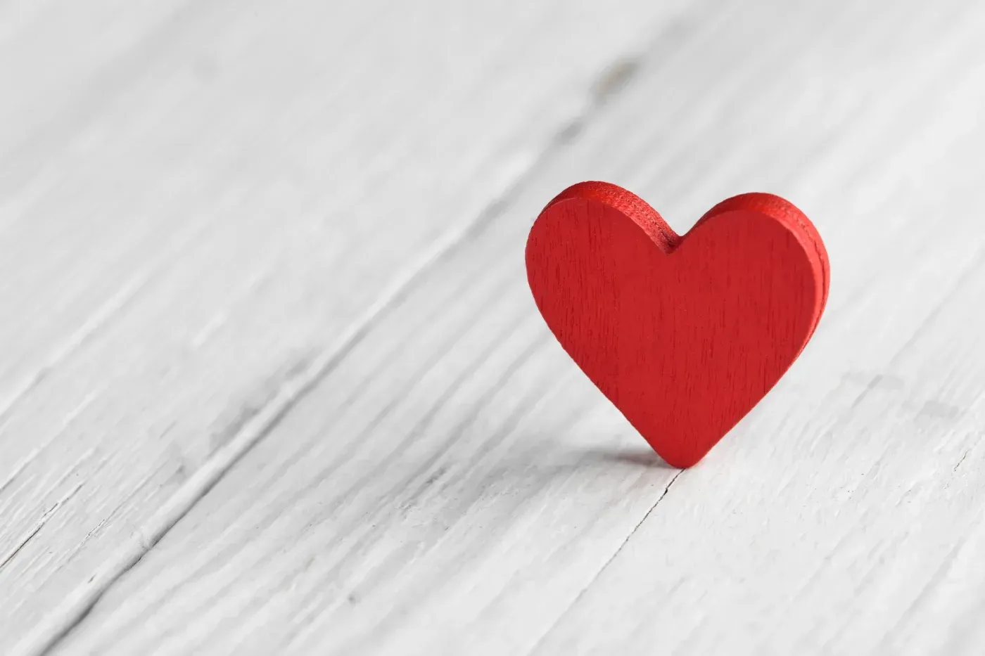 Red wooden heart standing on a whitewashed wood surface.