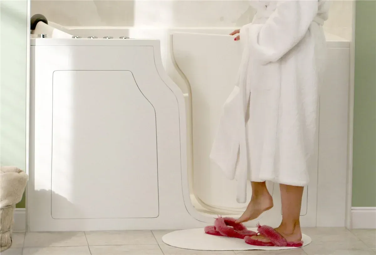 Person in white robe stepping into walk-in bathtub with open door, wearing pink slippers