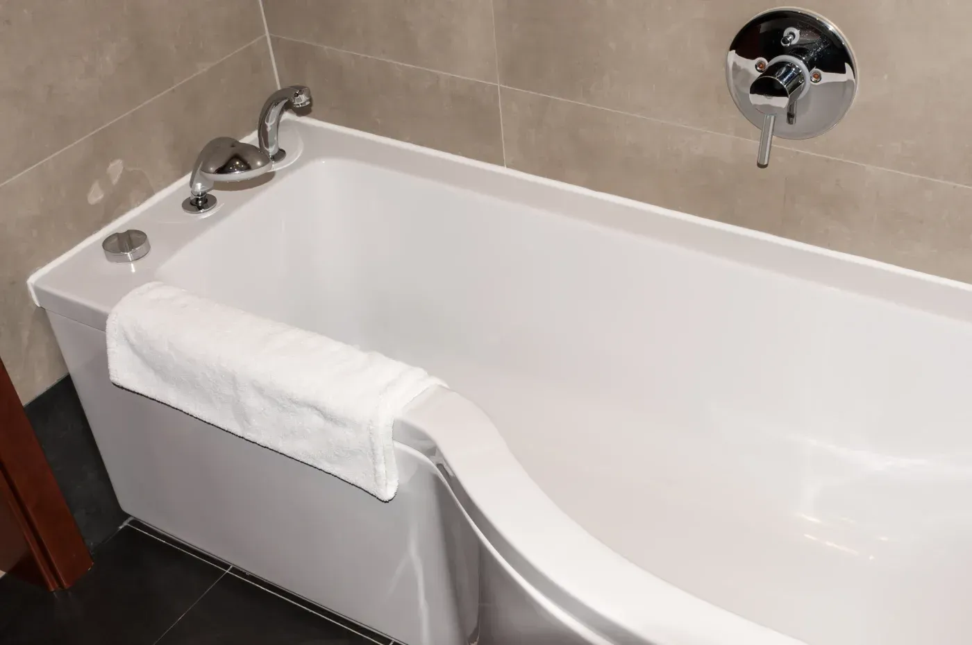 White soaking bathtub with chrome fixtures, beige tile walls, and a towel draped over the side.