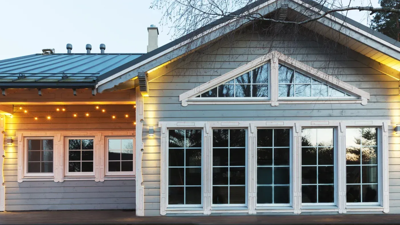 Gray house exterior with large grid-style windows, triangular clerestory windows, and warm accent lighting.