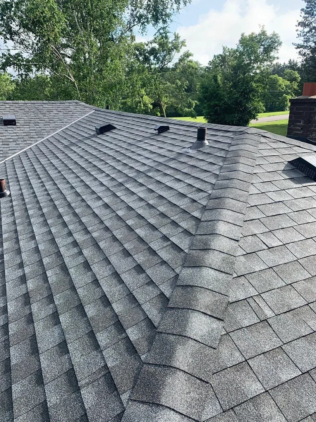 Newly installed gray asphalt shingle roof with multiple roof vents and skylights, overlooking tree-lined property