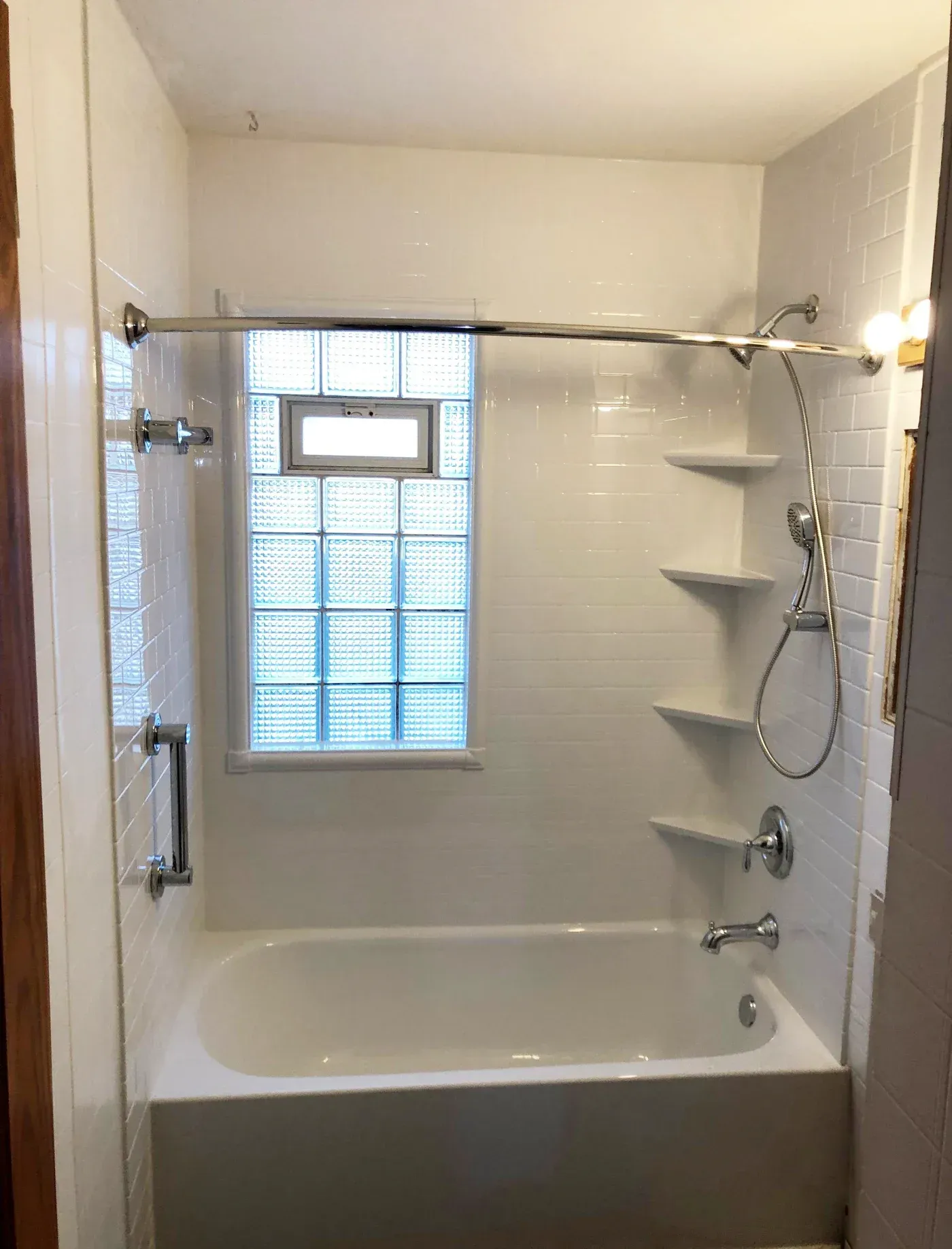 Bathroom with white subway tile walls, soaking tub, glass shower enclosure, rainfall showerhead, handheld shower, shelving, and glass block window
