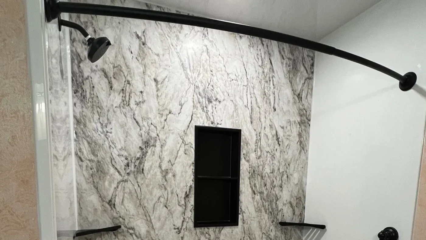 Bathtub and shower surround with marble-look wall panels, black shower fixtures, built-in shelving, and a curved shower curtain rod.