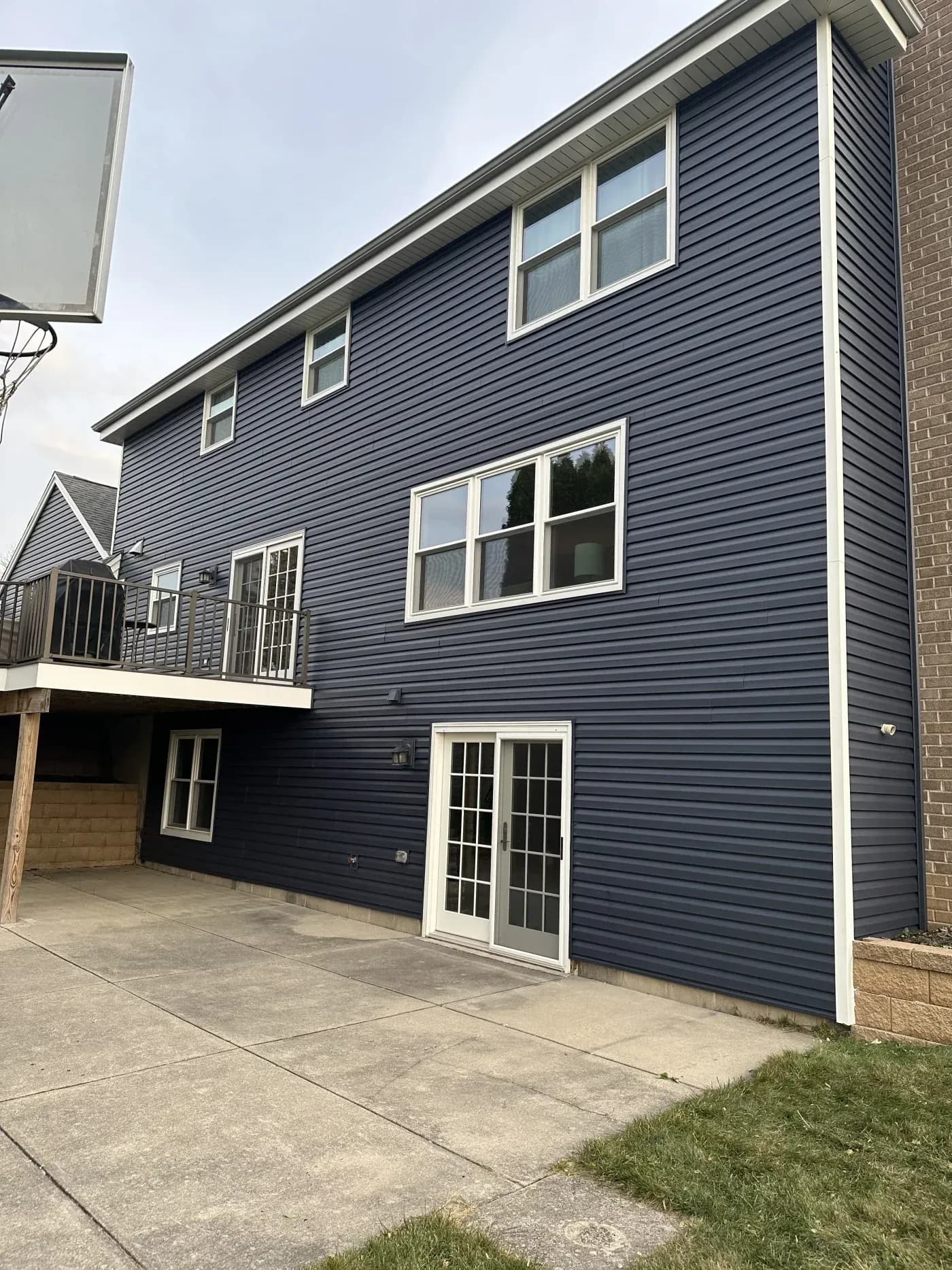 Two-story residential house with dark blue horizontal siding, white-trimmed windows, and a concrete driveway with an attached garage on the left side
