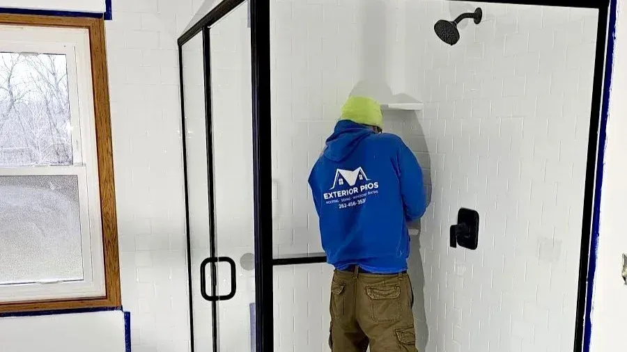 Exterior Pros installer finishing a new walk-in shower with white wall panels, black fixtures, and glass doors in Milwaukee, Wisconsin.