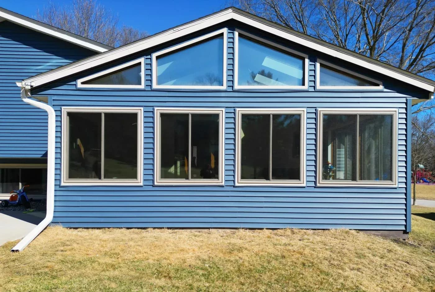 Large vinyl replacement windows with custom triangular transom windows on a blue-sided home in Menomonee Falls, Wisconsin.