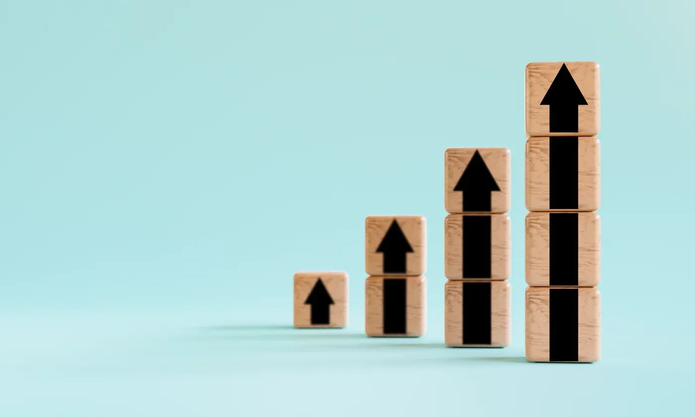Wooden blocks stacked in ascending columns with black upward arrows, symbolizing growth, progress, and improvement.