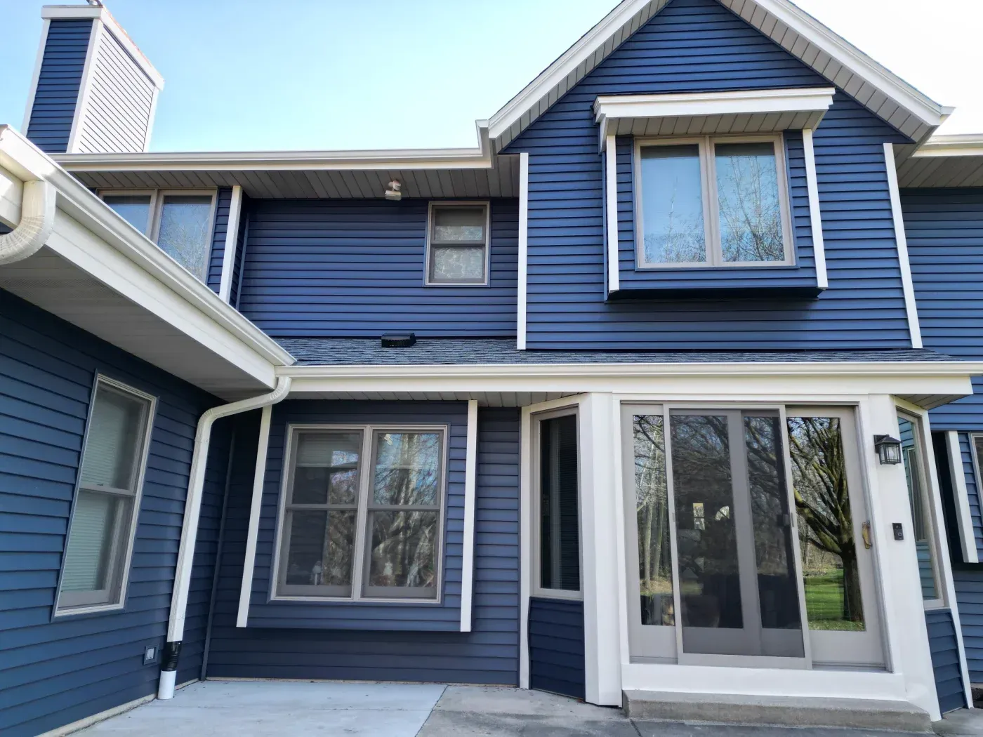 Two-story blue and white house with peaked roof, multiple windows, and attached garage on a clear day
