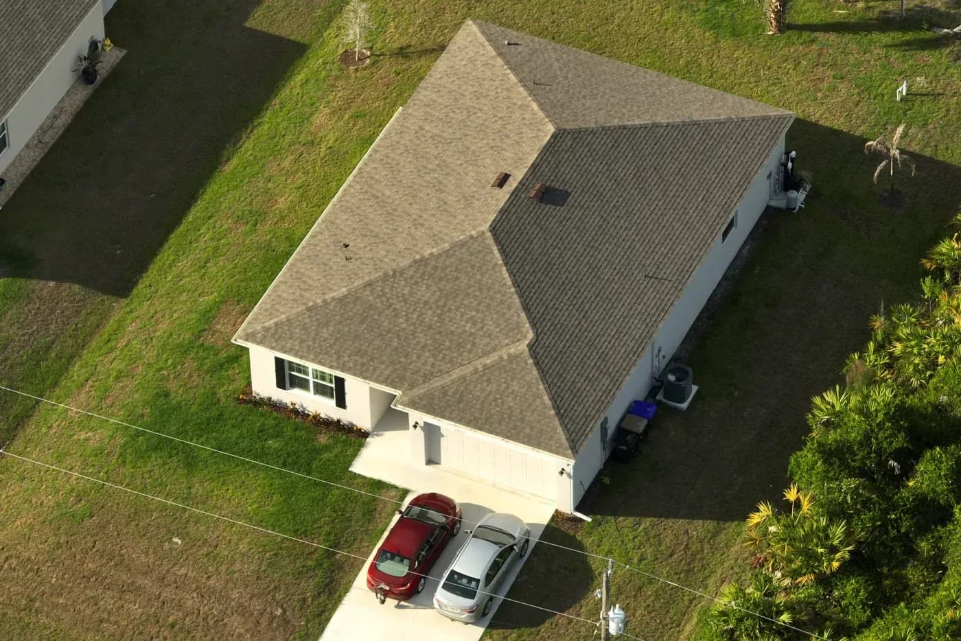Aerial view of a home with a tan asphalt shingle roof, attached garage, and driveway in Ashippun, Wisconsin.