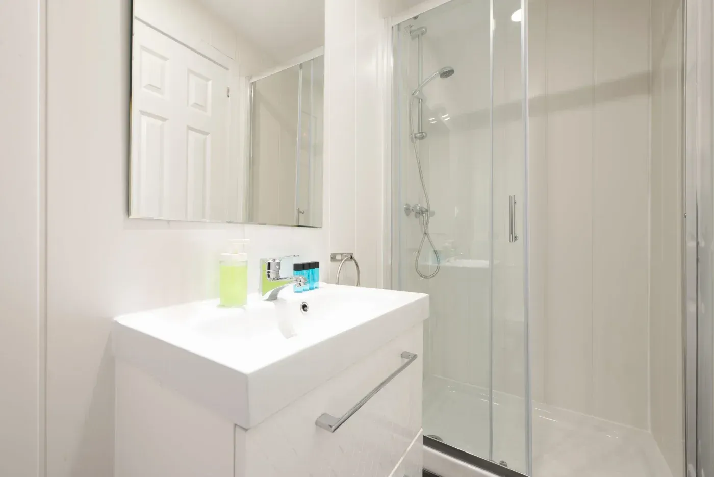 Bright white bathroom with a glass-enclosed walk-in shower, handheld showerhead, modern vanity, sink, and mirror in Adell, Wisconsin.