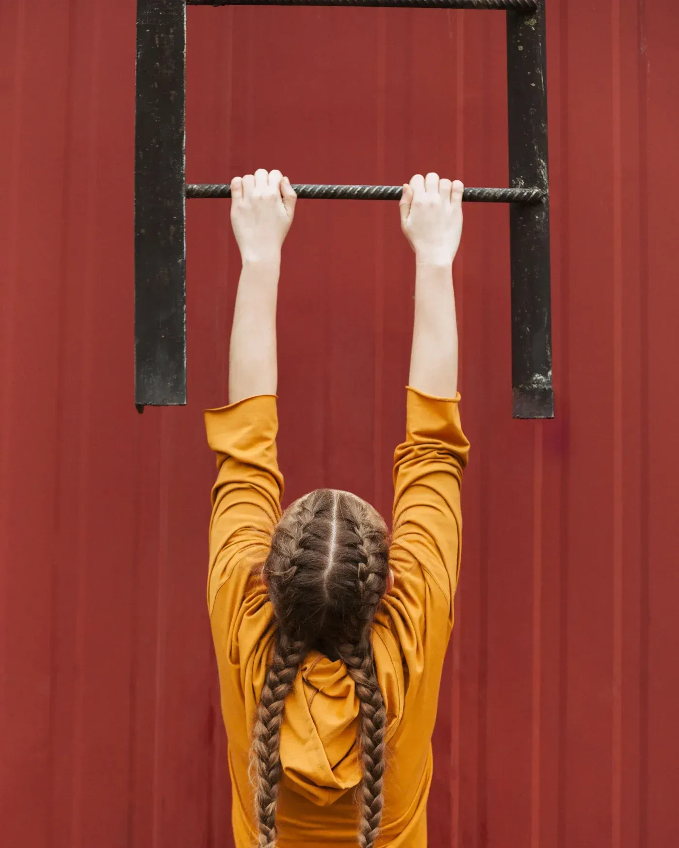 Person hanging from a black metal ladder against a red wall, illustrating strength and support for a wet-area bathroom remodeling project in Waukesha County, Wisconsin.